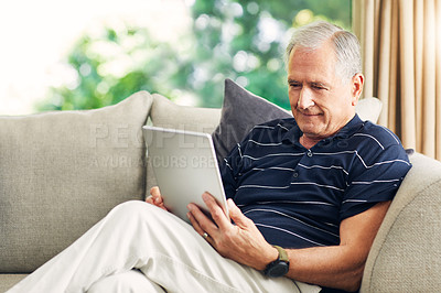 Buy stock photo Shot of a senior man using a digital tablet on the sofa at home