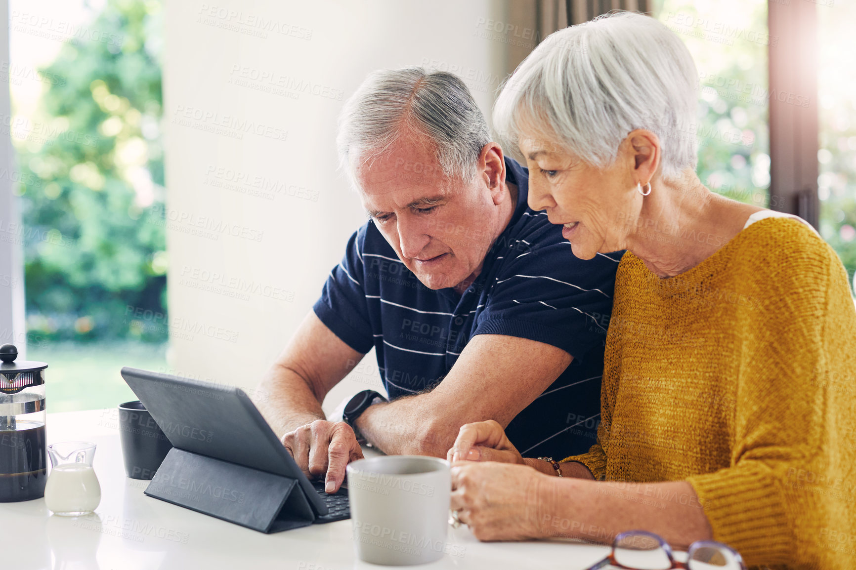 Buy stock photo Shot of a senior couple using a digital tablet and having coffee at home