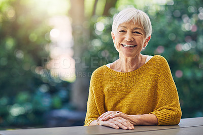 Buy stock photo Shot of a happy senior woman sitting at a table in her backyard