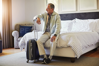 Buy stock photo Shot of a senior man sitting on a bed in his hotel room and looking thoughtful