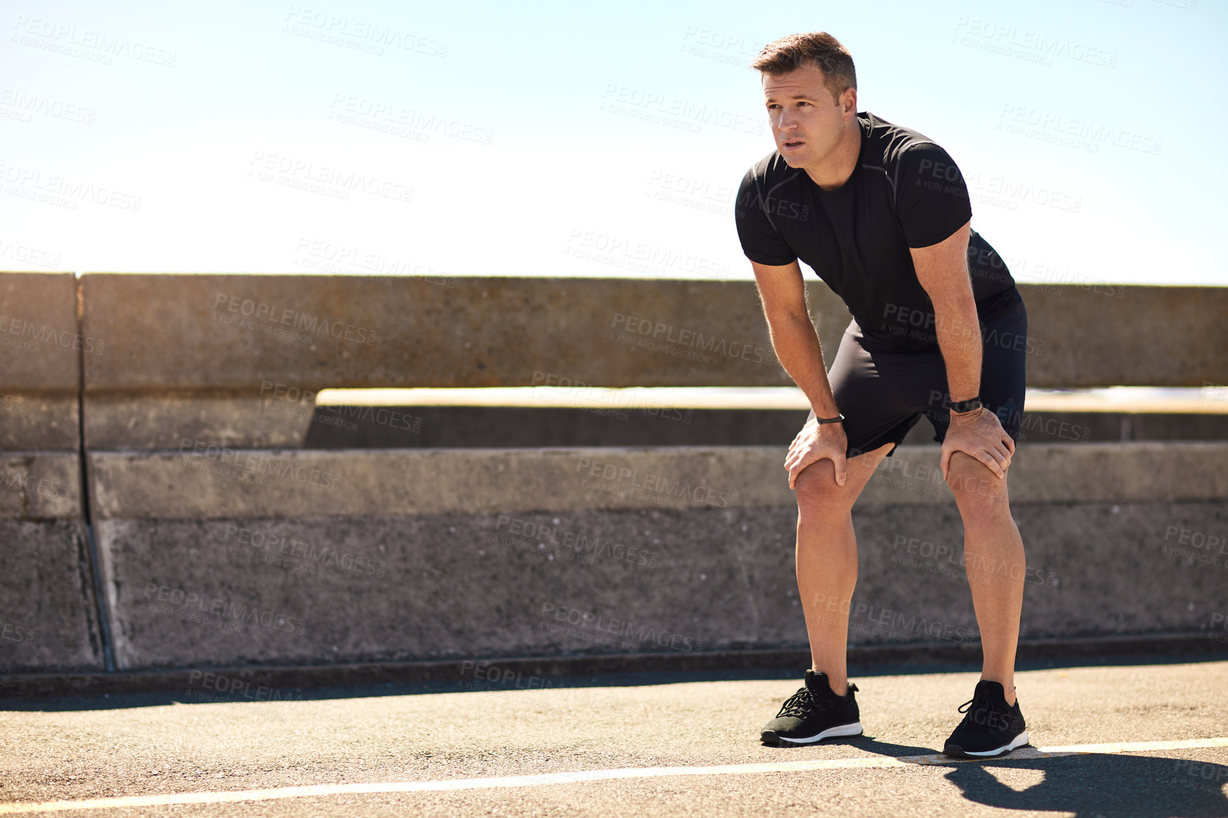 Buy stock photo Shot of a sporty young man out for a run on a bridge in the city