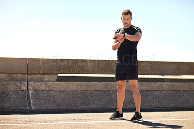 Buy stock photo Shot of a sporty young man looking at his wristwatch while out exercising