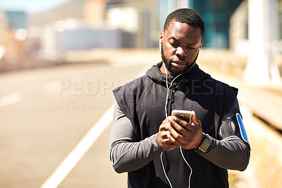 Buy stock photo Shot of a sporty young man using his cellphone while out for a run