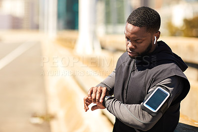 Buy stock photo Shot of a sporty young man looking at his wristwatch while out exercising