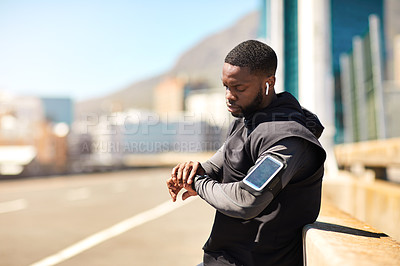 Buy stock photo Shot of a sporty young man looking at his wristwatch while out exercising