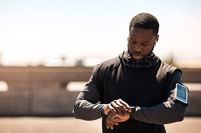 Buy stock photo Shot of a sporty young man looking at his wristwatch while out exercising