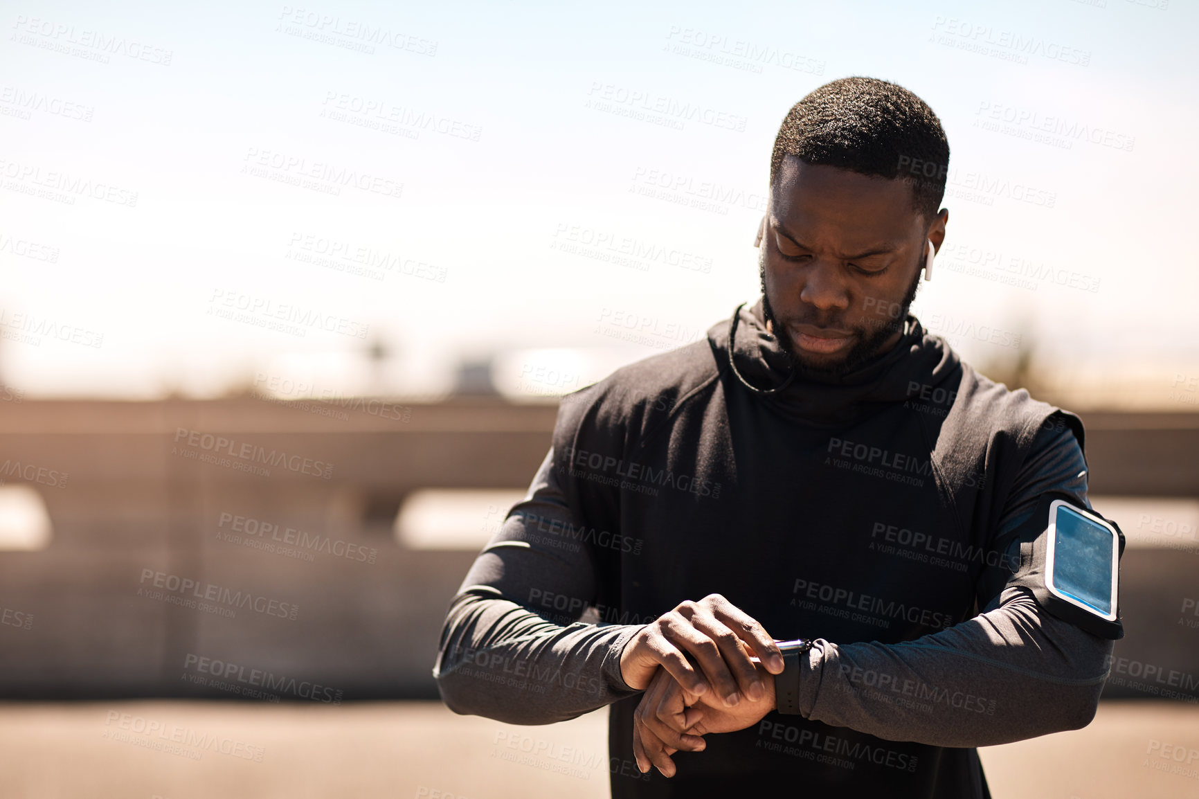 Buy stock photo Shot of a sporty young man looking at his wristwatch while out exercising