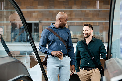 Buy stock photo Cropped shot of two businessmen talking while standing on an escalator in their office