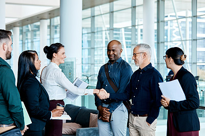 Buy stock photo Shot of two businesspeople shaking hands while their colleagues look on
