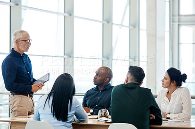 Buy stock photo Shot of a mature businessman using a digital tablet during a meeting with colleagues at work