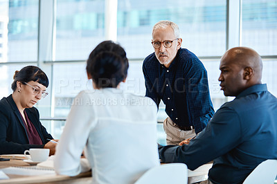 Buy stock photo Shot of a mature businessman looking serious during a meeting with colleagues at work