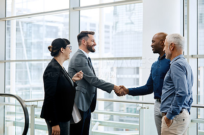 Buy stock photo Shot of two businessmen shaking hands while their colleagues look on