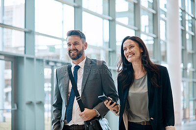 Buy stock photo Shot of two cheerful young businesspeople walking and having a conversation together at work
