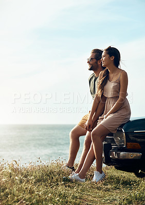 Buy stock photo Full length shot of an affectionate young couple holding hands while sitting on a car by the ocean