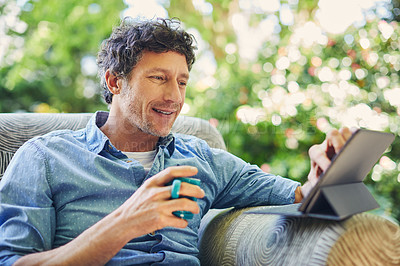 Buy stock photo Shot of a mature man relaxing in a chair while using a digital tablet and drinking coffee in his backyard