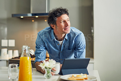 Buy stock photo Shot of a mature man looking thoughtful while having breakfast and using a digital tablet at home