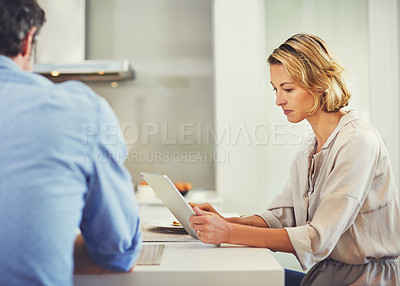Buy stock photo Shot of a mature woman using a digital tablet while having breakfast with her husband at home