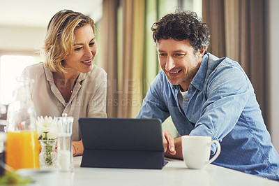 Buy stock photo Shot of a mature couple using a digital tablet while having breakfast at home
