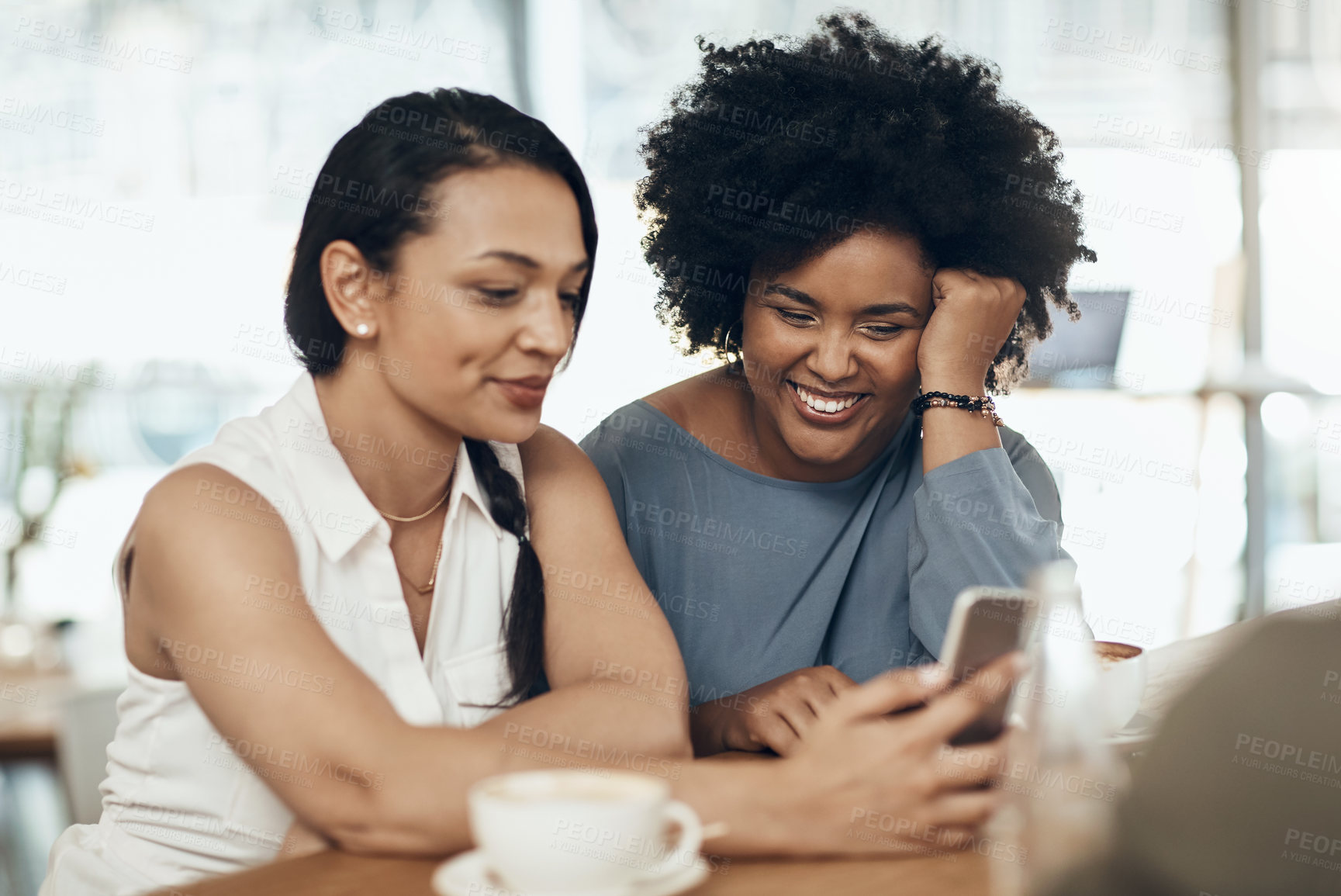 Buy stock photo Cropped shot of two attractive young women sitting together in a cafe and using a cellphone