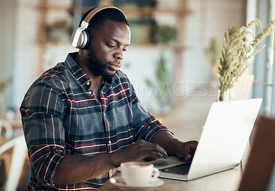 Buy stock photo Cropped shot of a handsome young businessman wearing headphones to listen to music and using his computer in a cafe
