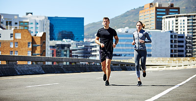 Buy stock photo Shot of two sporty young people out for a run in the city