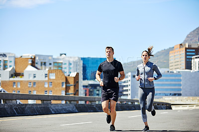 Buy stock photo Shot of two sporty young people out for a run in the city