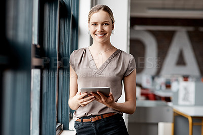 Buy stock photo Shot of an attractive young businesswoman standing alone in the office and using a digital tablet