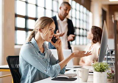 Buy stock photo Shot of a young businesswoman talking on a cellphone while working on a computer in an office