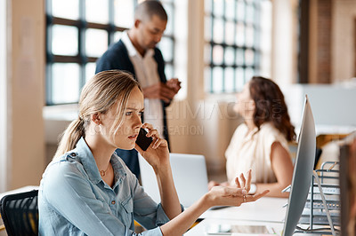 Buy stock photo Shot of a young businesswoman talking on a cellphone while working on a computer in an office