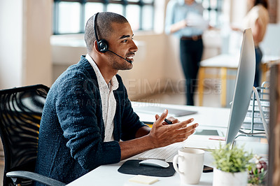 Buy stock photo Shot of a young businessman wearing a headset while working on a computer in an office