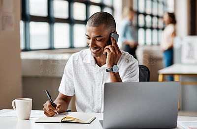 Buy stock photo Shot of a young businessman writing notes while talking on a cellphone in an office