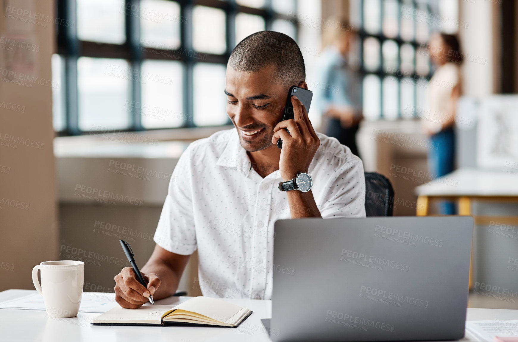 Buy stock photo Shot of a young businessman writing notes while talking on a cellphone in an office