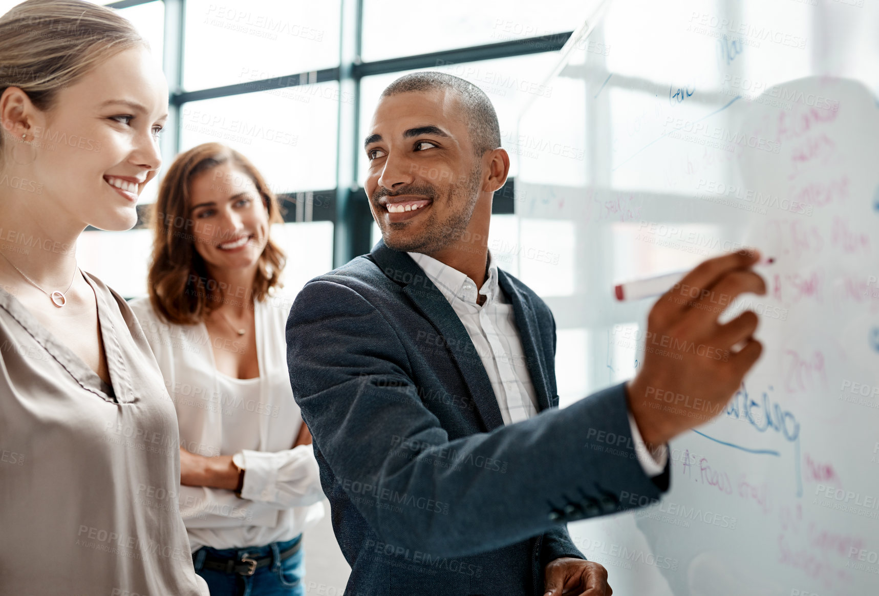 Buy stock photo Shot of a young businessman brainstorming on a whiteboard with his colleagues in an office
