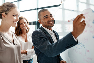 Buy stock photo Shot of a young businessman brainstorming on a whiteboard with his colleagues in an office