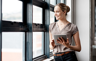 Buy stock photo Shot of a young businesswoman using a digital tablet while standing at a window in an office