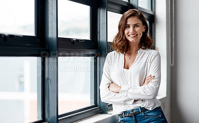 Buy stock photo Portrait of a confident young businesswoman standing at a window in an office