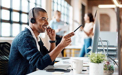 Buy stock photo Shot of a young man using a headset and computer in a modern office