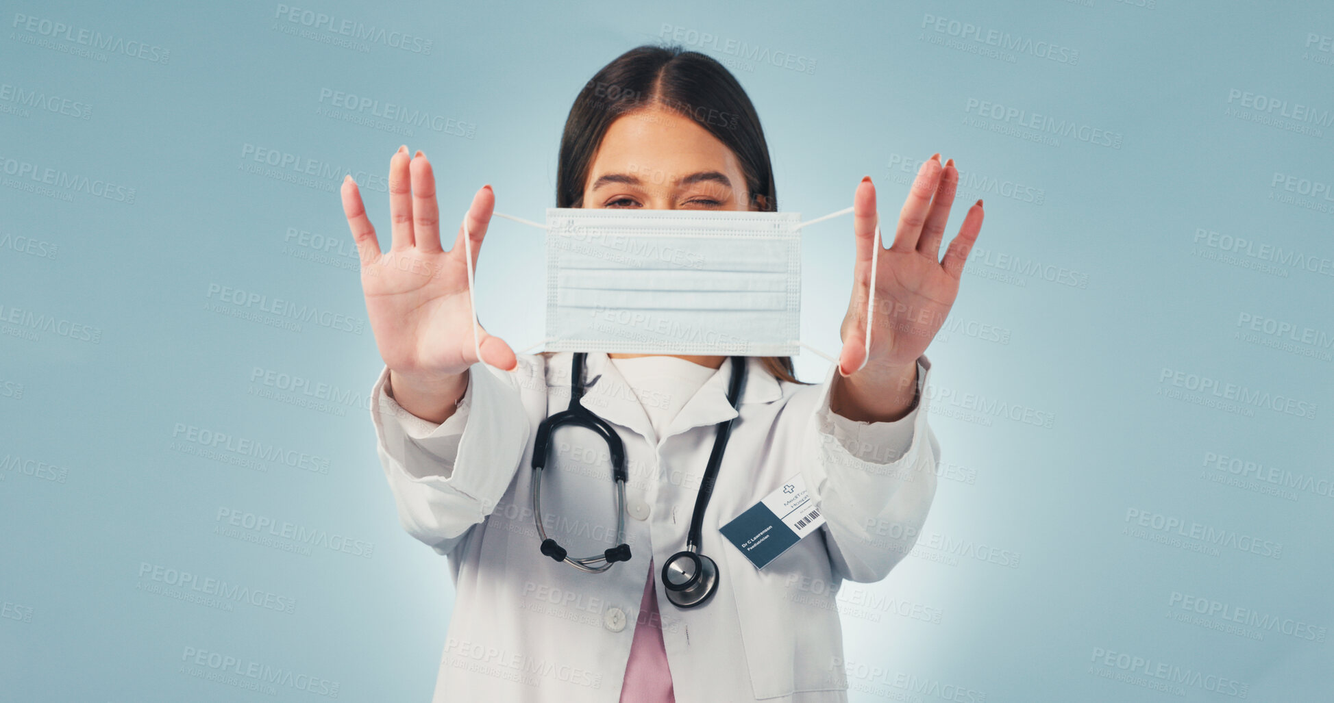 Buy stock photo Portrait, woman and doctor in studio with face mask, wink or infection control for virus prevention. Healthcare worker, playful person and medical rules for safety, PPE or protocol on blue background