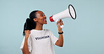 Volunteer, bullhorn and black woman in studio for awareness campaign on a blue background. Female person, helper or activist talking with megaphone speaker for alert, announcement or charity donation
