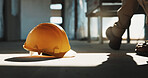 Safety, construction and helmet on floor with shoes of worker, protection compliance and engineering. Hard hat, gear and ppe with legs of person at site, development regulation and hazard prevention