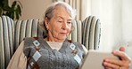 Tablet, reading and elderly woman on chair for online news, ebook or internet browsing. Retirement, old person or relax with digital tech in home for streaming subscription, puzzle or social media