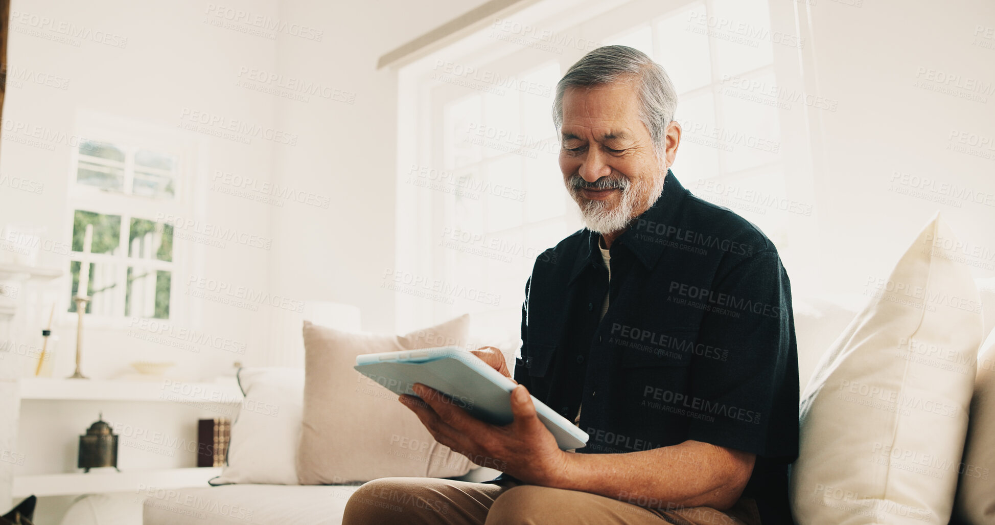 Buy stock photo Elderly, man and typing in living room with tablet, internet connection and browse website for ebook. Happy, senior Asian person and reading in home with tech, online story and retirement wellness.