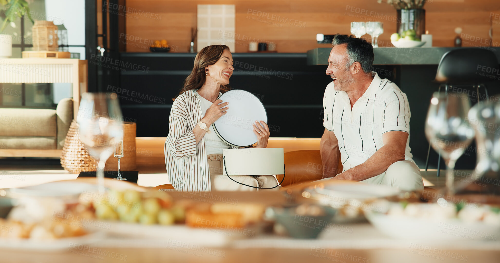 Buy stock photo Love, present and couple in house for thank you, laugh and anniversary celebration with smile. Mature man, woman and gift appreciation, gratitude or conversation with funny partner at romantic dinner