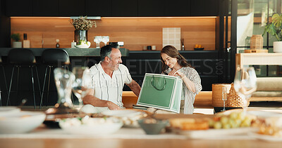 Buy stock photo Love, gift bag and mature couple in home, laugh and gratitude for anniversary celebration with smile. Man, woman and appreciation with present, care or marriage milestone with funny partner at lunch