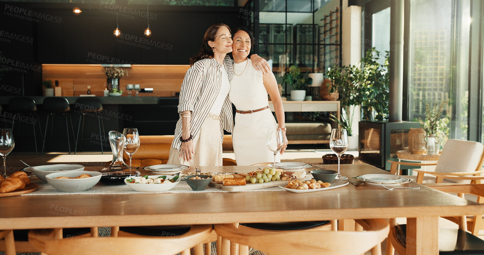 Buy stock photo Happy, friends and hug in home with meal, bonding together  or visit for connection on weekend break. Portrait, mature women and embrace by dining table with lunch food, care or smile for friendship.