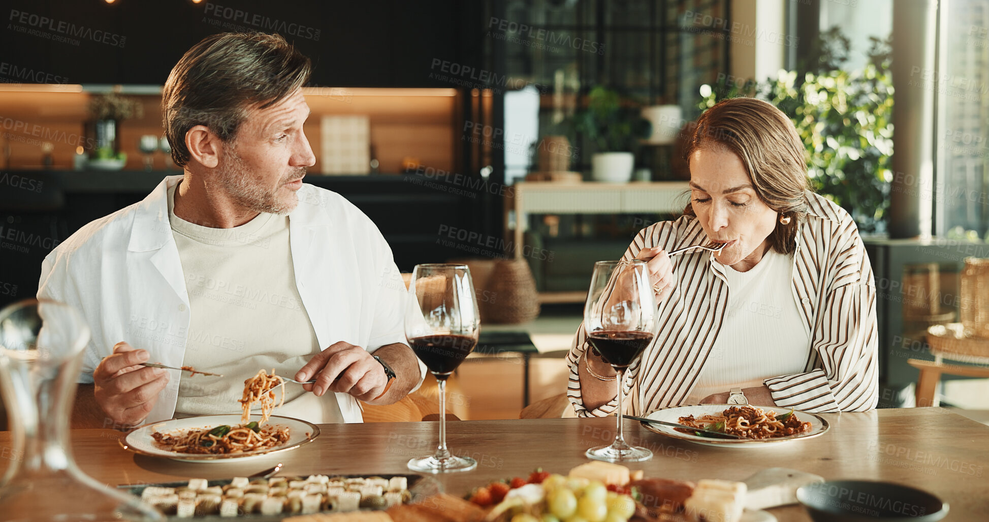 Buy stock photo Couple, lunch and conversation at dining table with wine, relax together and gossip on weekend break. Mature people, date and eating spaghetti food in home with alcohol drink, bonding and discussion.