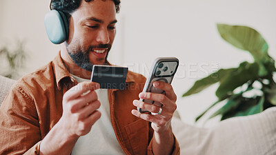 Buy stock photo Man, credit card and headphones or phone on home sofa for streaming music, shopping or subscription. Happy, online movie and person relax on couch with payment, technology and membership purchase