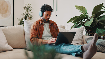 Buy stock photo Man, typing and headphones or laptop on home sofa for streaming music, podcast or subscription. Serious, online movie and male person relax on couch with website, technology and search series