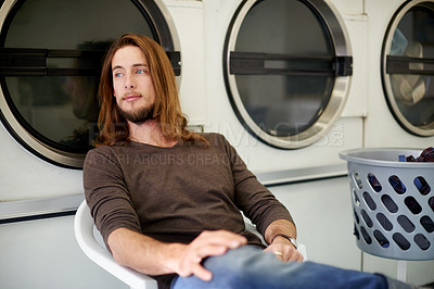 Buy stock photo Laundromat, man and waiting with clothes for washing, machine and customer with thinking on weekend. Self service facility, male person and relax with thoughts for cleaning laundry, basket or hygiene