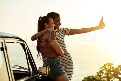 Buy stock photo Shot of two young women taking selfies with a mobile phone on a road trip